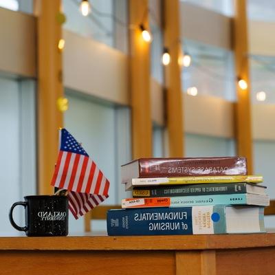 A stack of books and Oakland University on a desk.